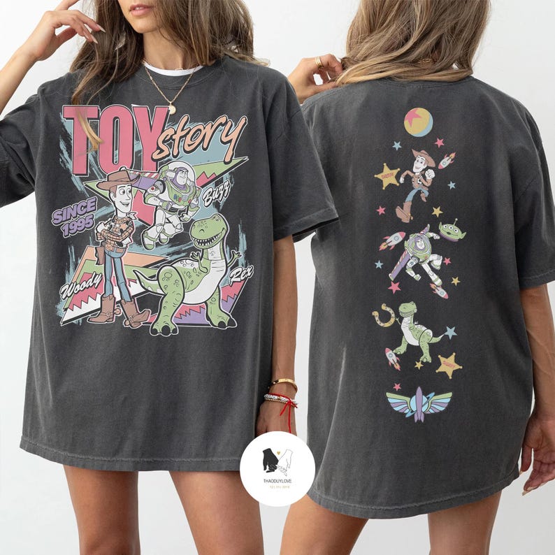 May include: Dark gray t-shirt featuring the words "Toy Story" with Woody, Buzz Lightyear, and Rex the dinosaur. The back of the shirt has a vertical design with various Toy Story characters and a colorful moon and stars.