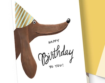 Könnte beinhalten: Geburtstagskarten mit einem braunen Dackel mit Partyhut. Auf der Vorderseite der Karte steht in schwarzer Schrift "Happy Birthday to you!". Der Umschlag ist gelb, und die Innenseite der Karte hat eine passende Illustration.