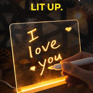 May include: A glowing acrylic sign with the words "I love you" written on it, illuminated by a warm light. The sign is mounted on a wooden base. The text "YOUR WORDS, LIT UP" is at the top.