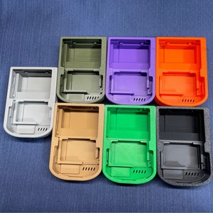 K&ouml;nnte beinhalten: Acht verschiedene farbige Plastikh&uuml;llen f&uuml;r ein Handheld-Spieleger&auml;t. Die H&uuml;llen sind in einem Kreis angeordnet, wobei die Oberseite jeder H&uuml;lle zum Betrachter zeigt. Die Farben der H&uuml;llen sind grau, gr&uuml;n, orange, lila, braun, schwarz und zwei Gr&uuml;nt&ouml;ne.