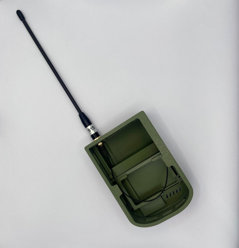 K&ouml;nnte beinhalten: Ein gr&uuml;nes, offenes Handger&auml;t mit einer schwarzen Antenne und einem Etikett mit der Aufschrift "915".