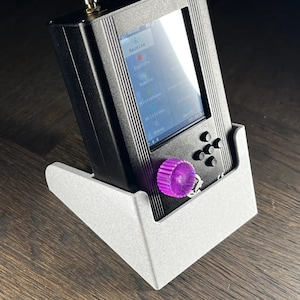 Könnte beinhalten: Ein schwarzes Handgerät mit einem Farbbildschirm, auf dem der Text "Empfangen", "Aufnehmen", "Fernmikrofon" und "Dienstprogramme" angezeigt wird. Das Gerät steht in einem weißen 3D-gedruckten Ständer.