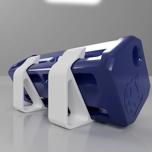 May include: A dark blue rectangular object with a white cat logo on one side. The object is sitting on two white triangular supports.