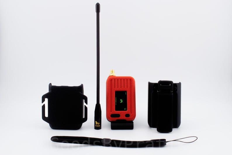 May include: A red handheld radio transmitter with a black antenna, a black wrist strap, and a black carrying case. The radio has a small screen with a green symbol on it.