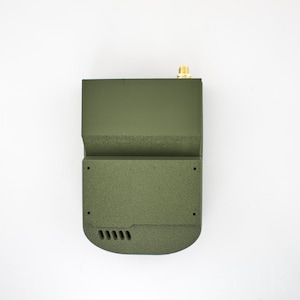 K&ouml;nnte beinhalten: Ein gr&uuml;nes, rechteckiges elektronisches Ger&auml;t mit einer kleinen Antenne oben. Das Ger&auml;t hat eine strukturierte Oberfl&auml;che und eine Reihe kleiner L&ouml;cher unten.