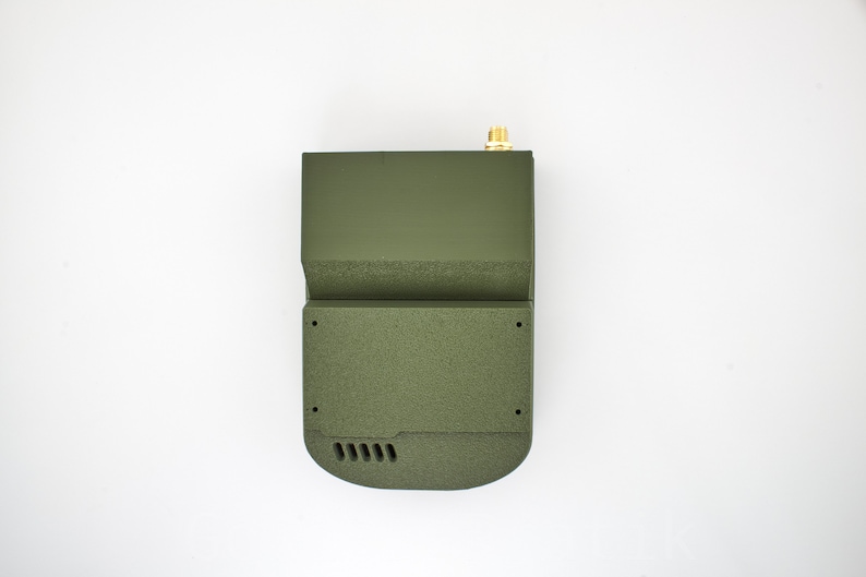 K&ouml;nnte beinhalten: Ein gr&uuml;nes, rechteckiges elektronisches Ger&auml;t mit einer kleinen Antenne oben. Das Ger&auml;t hat eine strukturierte Oberfl&auml;che und eine Reihe kleiner L&ouml;cher unten.