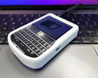 Könnte beinhalten: Eine weiße und blaue Tastatur mit einem kleinen Bildschirm und einer Antenne. Auf dem Bildschirm wird der Text "keyboard.org" angezeigt. Die Tastatur liegt auf einer silbernen Laptop-Tastatur.