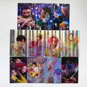 May include: A collection of eleven rectangular trading cards featuring stylized digital illustrations of characters with diverse hair colors and outfits. The cards have a holographic finish that creates a shimmering, rainbow-like light effect.