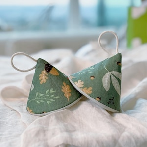 May include: Two green fabric pot holders with a white trim and a pattern of leaves, acorns, and branches. The pot holders have a loop of white fabric for hanging.