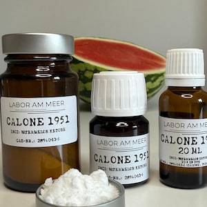 Peut inclure: Trois flacons en verre ambré avec des étiquettes et des couvercles blancs, étiquetés "CALONE 1951" et "WATERMELON KETONE". Un petit plat contient de la poudre blanche. Une tranche de pastèque est en arrière-plan.