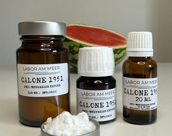 Puede incluir: Tres frascos de vidrio ámbar con etiquetas blancas que dicen Labor Am Meer Calone 1951 Inci: Watermelon Ketone, un pequeño recipiente de metal lleno de polvo blanco y una sandía cortada por la mitad al fondo. Los frascos tienen tapas plateadas y blancas.