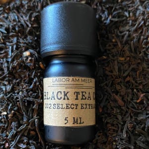 May include: A small black bottle with a brown label that reads "LABOR AM MEER BLACK TEA CO2 SELECT EXTRACT 5 ML". The bottle is sitting on a bed of loose black tea leaves.