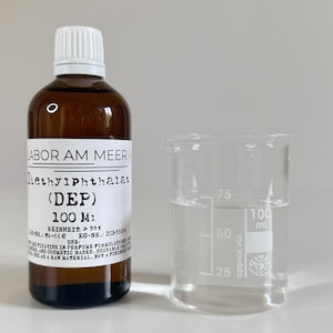 May include: A brown glass bottle with a white cap and a clear beaker. The bottle has a label with text including "Diethylphthalat (DEP) 100 M1". The beaker contains a clear liquid, with volume markings.