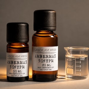 May include: Two amber glass bottles with black caps and white labels, alongside a small glass beaker. The bottles are labeled "AMBERMAX 50%TPM" with 10 ml and 20 ml volumes. The beaker contains a clear liquid, with 10 ml markings.