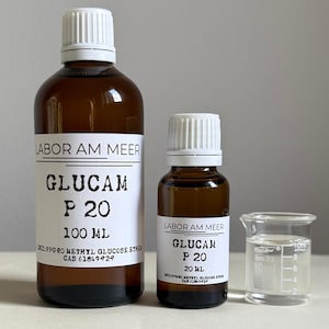 Può includere: Due bottiglie di vetro marrone con etichette e tappi bianchi e un piccolo becher. Le etichette riportano "LABOR AM MEER" e "GLUCAM P 20", con misure di volume di 100 ml e 20 ml. Il becher contiene un liquido trasparente.