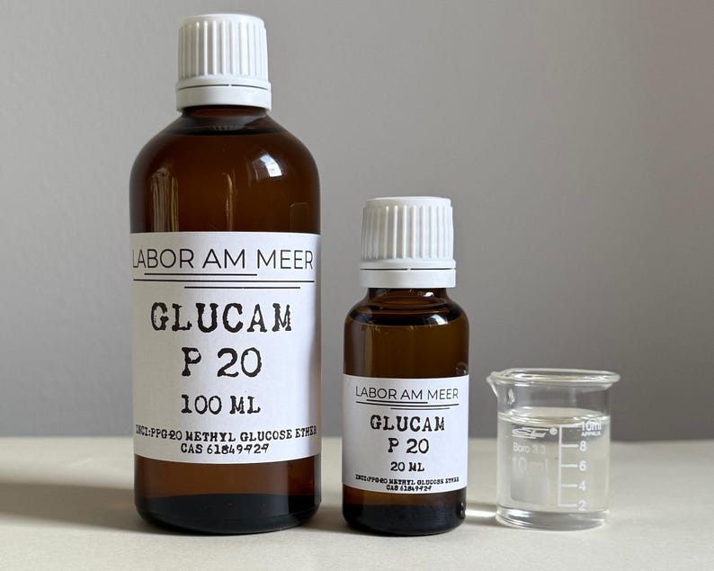 May include: Two brown glass bottles with white labels and caps, and a small beaker. The labels read "LABOR AM MEER" and "GLUCAM P 20", with volume measurements of 100 mL and 20 mL. The beaker contains a clear liquid.