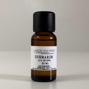 May include: A small amber glass bottle with a black cap. The label reads "LABOR AM MEER" and "COUMARIN 10% IN DPG 20 ml." The bottle contains a brown liquid. The bottle is approximately 3 inches tall.