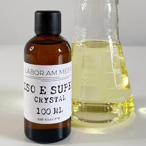 Może przedstawiać: Brązowa szklana butelka z czarną zakrętką i białą etykietą z napisem "LABOR AM MEER ISO E SUPER CRYSTAL 100 ML". Obok niej przezroczysty szklany zlewka zawierająca ż&oacute;łty płyn.