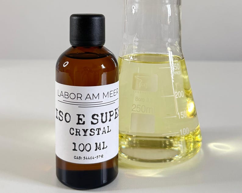 Może przedstawiać: Brązowa szklana butelka z czarną zakrętką i białą etykietą z napisem "LABOR AM MEER ISO E SUPER CRYSTAL 100 ML". Obok niej przezroczysty szklany zlewka zawierająca ż&oacute;łty płyn.