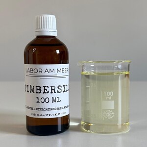 May include: A brown glass bottle with a white cap and a label that reads "TIMBERSIL 100 ml" next to a 100 ml beaker filled with a clear liquid. The label also includes the text "LABOR AM MEER".