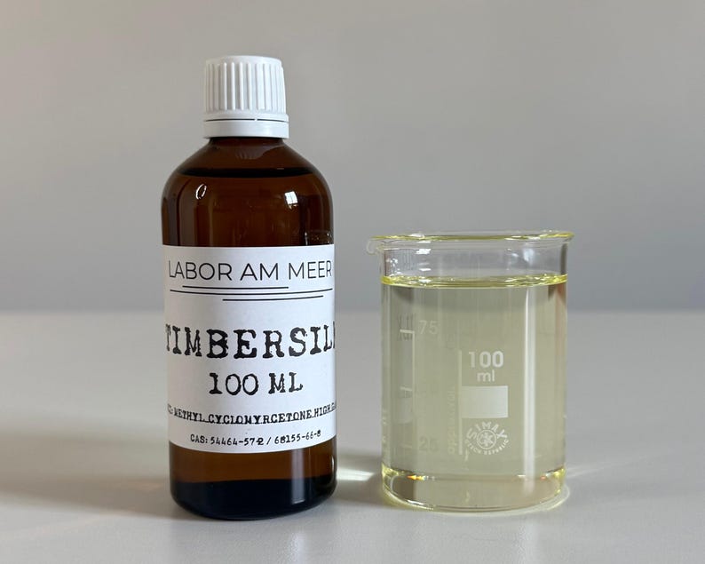 May include: A brown glass bottle with a white cap and a label that reads "TIMBERSIL 100 ml" next to a 100 ml beaker filled with a clear liquid. The label also includes the text "LABOR AM MEER".