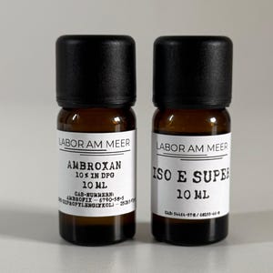 Può includere: Due piccoli flaconi di vetro ambrato con tappi neri. Ogni flacone ha un'etichetta bianca con testo nero. Uno recita "AMBROXAN 10% IN DPG 10 ml" e l'altro "ISO E SUPER 10 ml". Il testo "LABOR AM MEER" è sopra le etichette.
