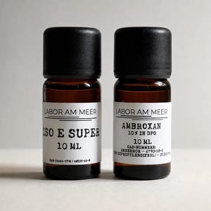 May include: Two amber glass bottles with black screw-on caps, each containing 10 ml of liquid. The white labels feature the text LABOR AM MEER, with one bottle labelled ISO E SUPER and the other labelled AMBROXAN 10% IN DPG, including CAS numbers.