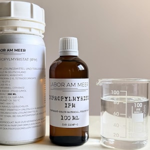 May include: Three laboratory containers are shown: two bottles and a beaker. The bottles, labelled "LABOR AM MEER", contain "ISOPROPYLMYRISTAT (IPM)". One bottle is clear, the other amber. A clear beaker with liquid is next to the bottles. The amber bottle is 100 ml.