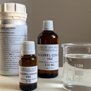 May include: A collection of laboratory chemicals, featuring three bottles and a beaker. The bottles are labelled with "TRIETHYL CITRATE TEC" and measurements such as 20 ml and 100 ml. The beaker is filled with a clear liquid.