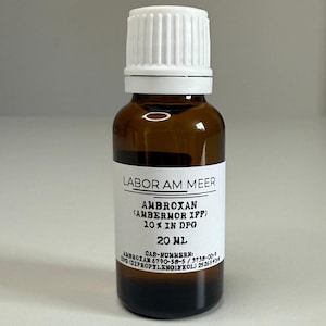 May include: A brown glass bottle with a white cap and a white label. The label reads "LABOR AM MEER" and "AMBROXAN (AMBERMOR IFF) 10% IN DPG 20 mL". The bottle contains a dark liquid.