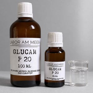 Może przedstawiać: Dwie butelki z brązowego szkła z białymi zakrętkami i białymi etykietami z napisem Labor Am Meer Glucam P 20, o pojemności 100 ml i 20 ml, obok małej przezroczystej szklanej zlewki z podziałką do 10 ml, wszystkie zawierające przezroczysty płyn.