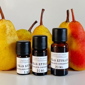 Può includere: Tre piccole bottiglie di vetro con tappi neri etichettate "Estratto di Pera, Concentrato di Fragranza" sono esposte davanti a pere mature. Le bottiglie sono etichettate 5 ml, 10 ml e 20 ml. Le pere sono gialle e rosse.