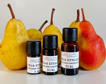 Puede incluir: Tres pequeños frascos de vidrio con tapas negras etiquetados "Extracto de Pera, Concentrado de Fragancia" se muestran frente a peras maduras. Las botellas están etiquetadas 5 ml, 10 ml y 20 ml. Las peras son amarillas y rojas.