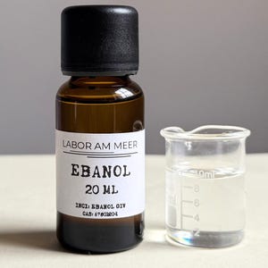 May include: A brown glass bottle with a black cap and a white label that reads "LABOR AM MEER EBANOL 20 ml". Next to it is a small glass beaker with a clear liquid inside.