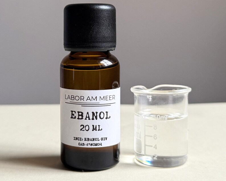 May include: A brown glass bottle with a black cap and a white label that reads "LABOR AM MEER EBANOL 20 ml". Next to it is a small glass beaker with a clear liquid inside.