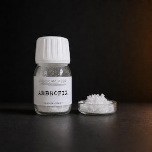 May include: A clear glass bottle with a white ribbed cap and a white label reading LABOR AM MEER AMBROFIX CAS: 6790-58-5, 3738-00-9, containing white crystalline powder. Next to the bottle is a small glass dish filled with the same white crystals.