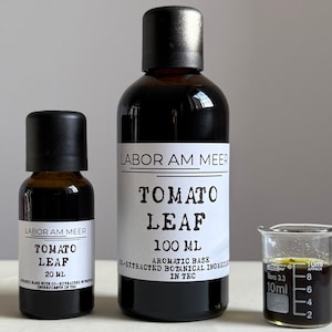 Könnte beinhalten: Drei dunkle Glasflaschen mit schwarzen Verschlüssen und weißen Etiketten. Die Etiketten lauten "LABOR AM MEER TOMATO LEAF" mit den Größen 20 ml und 100 ml. Ein kleiner Becher enthält eine dunkle Flüssigkeit. Botanisches Produkt.