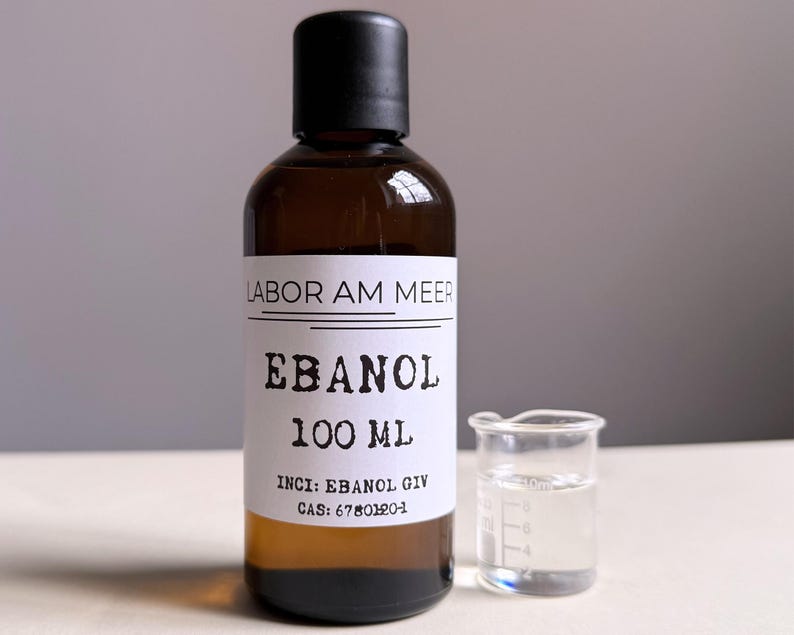 May include: A brown glass bottle with a black cap and a white label that reads "LABOR AM MEER EBANOL 100 ML". A small glass beaker with liquid is next to the bottle.
