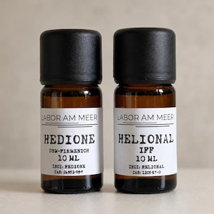 Può includere: Due flaconi in vetro ambrato con tappi neri a vite, contenenti ciascuno 10 ml di liquido. Le etichette bianche riportano la scritta LABOR AM MEER, con un flacone etichettato HEDIONE DSM-FIRMENICH e l'altro HELIONAL IFF, inclusi i codici INCI e CAS.