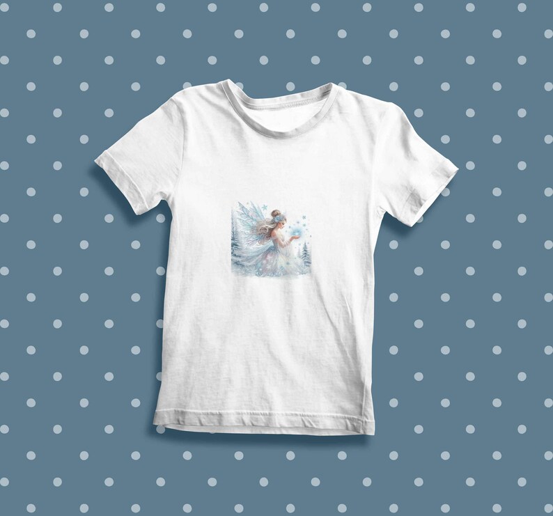 May include: White t-shirt with a watercolor illustration of a fairy holding a snowflake in a snowy forest setting.