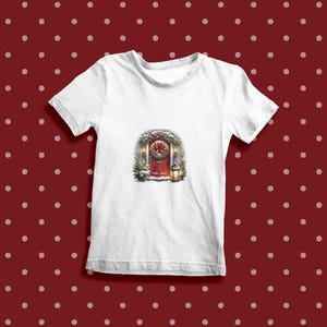 May include: White t-shirt with a Christmas-themed image of a red door with a wreath, lights, and snow.