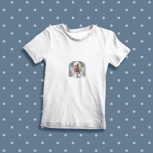 May include: White t-shirt featuring a colourful illustration of a girl in a red dress and a white hat holding a gift in a snowy forest scene.