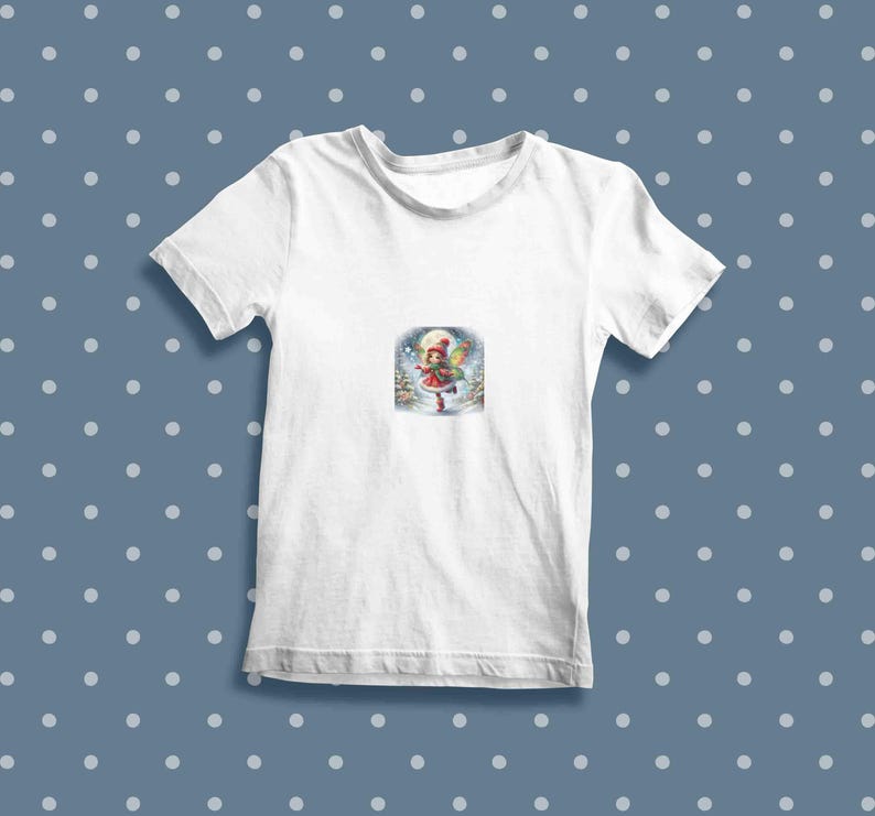 May include: White t-shirt featuring a colourful illustration of a girl in a red dress and a white hat holding a gift in a snowy forest scene.