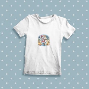 May include: White t-shirt with a colorful illustration of a fairy holding a snowman in a winter scene.