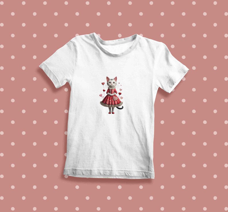 May include: White t-shirt with a graphic of a cat wearing a red dress and holding a heart. The cat is surrounded by pink hearts.