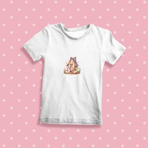 May include: White t-shirt with a colorful illustration of a small house with a birdhouse on top.  The house is surrounded by colorful eggs and small chicks.