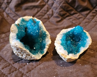 May include: Two geode halves with a white exterior and a blue crystal interior. The geodes are sitting on a brown surface.
