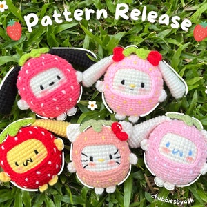 May include: Five crocheted strawberry-themed plushies with different facial expressions. The plushies are in various colors, including pink, red, and yellow. The plushies are arranged on a bed of green grass. The text "Pattern Release" is written in white letters on a black background above the plushies.