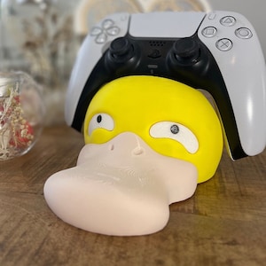Könnte beinhalten: Ein gelber und weißer Enten-Controller-Ständer für einen weißen PlayStation 5-Controller.