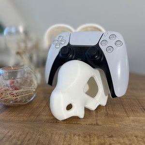 Könnte beinhalten: Weißer und schwarzer Videospiel-Controller, der in einem weißen 3D-gedruckten Schädelständer ruht.